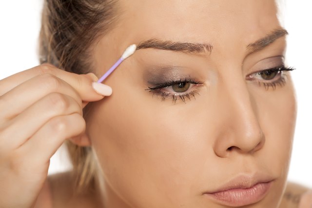 Young woman contouring her eyebrows with cotton swab on white background