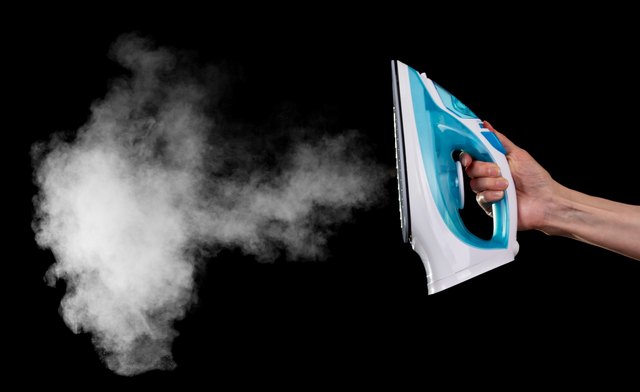 Steam iron in female hand isolated on black background.