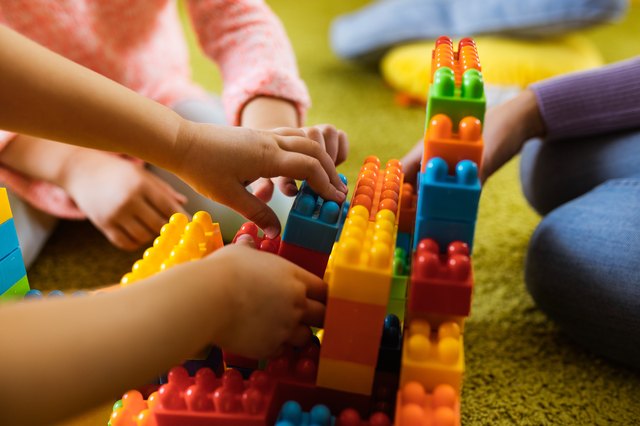 Close up of unrecognizable kids playing with toy blocks on carpet.