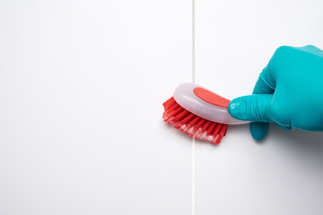 Male hand with red brush cleaning the bathroom tiles and gaps. Before and after effect.