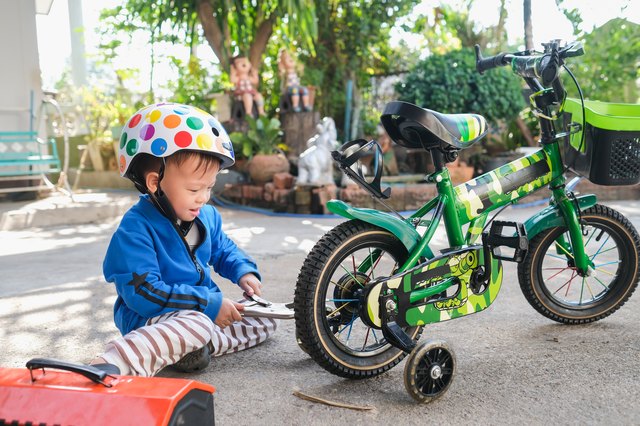Cute happy smiling little Asian 2 - 3 years old toddler boy child wearing safety helmet repairing bicycle wheel with spanner