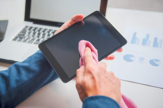 Cropped Hand Of Businessman Cleaning Digital Tablet Screen At Desk In Office
