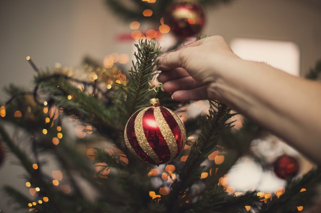 Woman holding Christmas bauble in front of illuminated Christmas tree