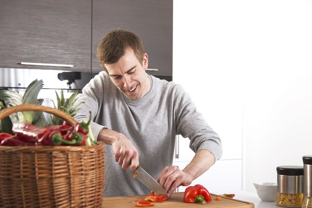 Junger Mann beim Paprika schneiden in Küche
