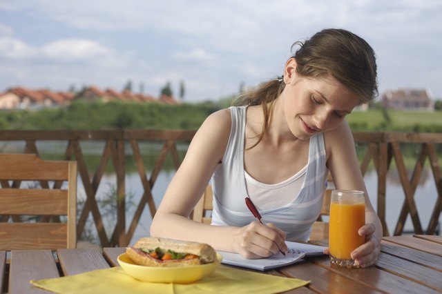 Woman eating and sitting on terrace writing