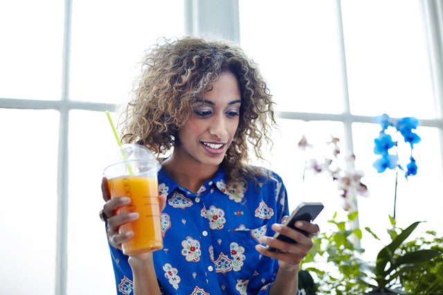 Mixed race woman drinking smoothie using her phone