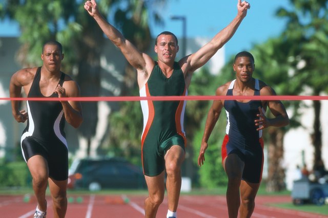 portrait of a young male athlete crossing the finish line first with his arms raised up in victory