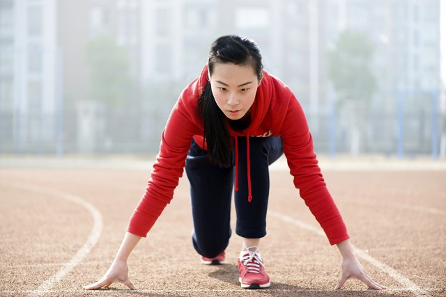 Athletic Asian woman in start position on track