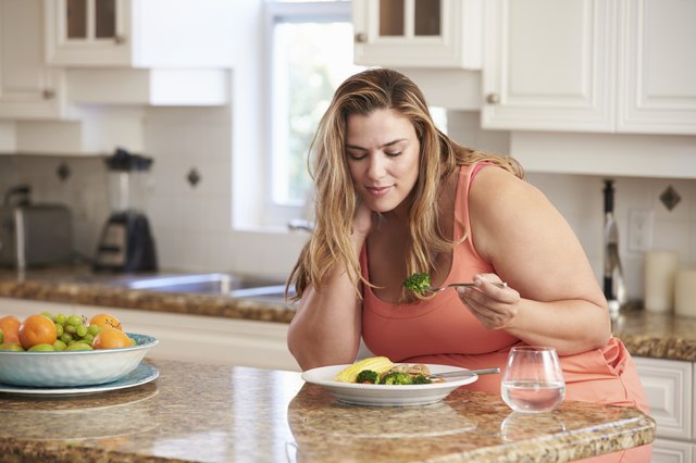 Overweight Woman Eating Healthy Meal In Kitchen