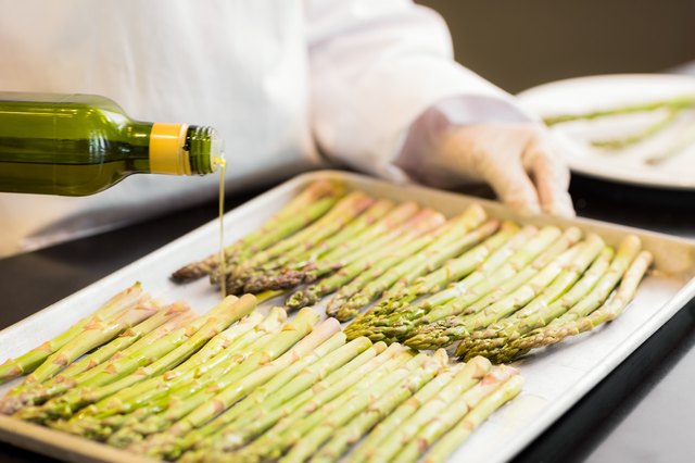 Hand pouring oil on fresh asparagus