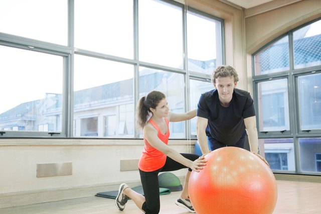 Fitness trainer helping young man with exercises on a fitness ball