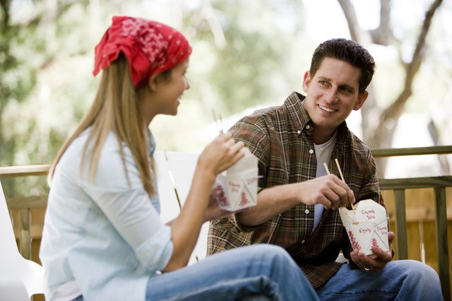 Cheerful young couple eating noodles on armchairs