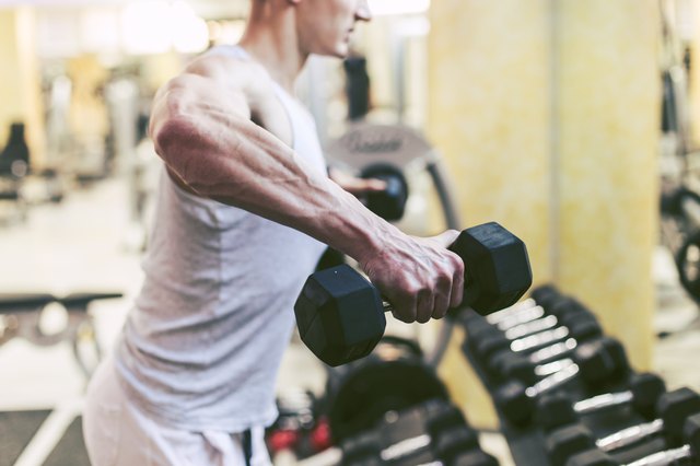 Muscular Bodybuilder Doing Exercises with Dumbbells in Gym
