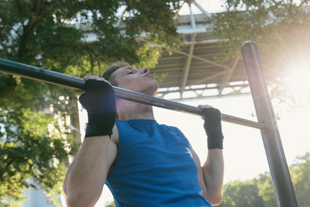 Young man exercising, doing pull-ups on bar