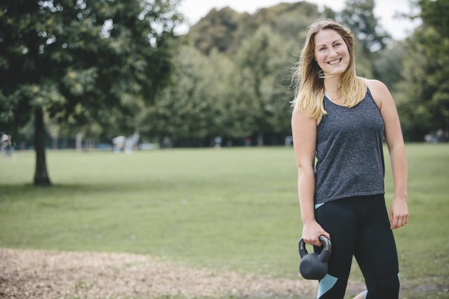 Smiling young woman holding kettlebell in park