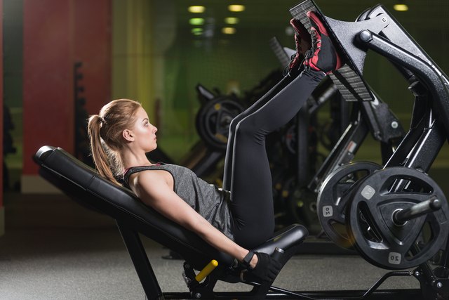 Sportive woman using weights press machine for legs. Gym.