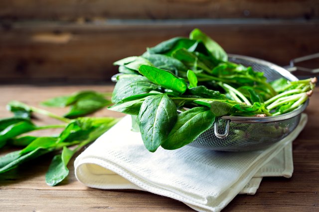 Wet spinach leaves in sieve wooden background