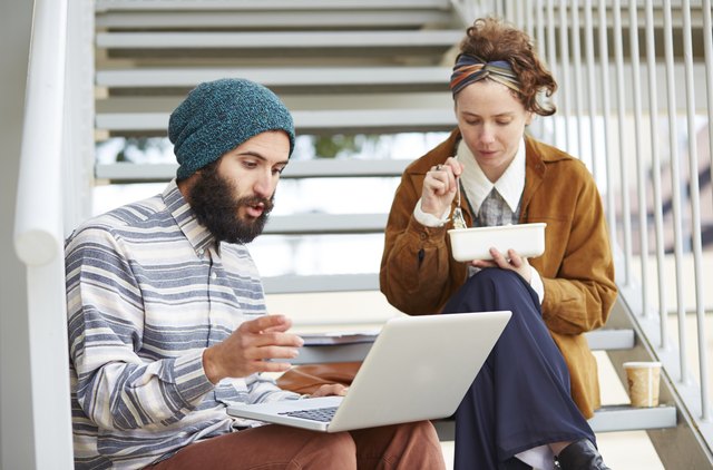 Hipster couple using computer and eating lunch outdoors