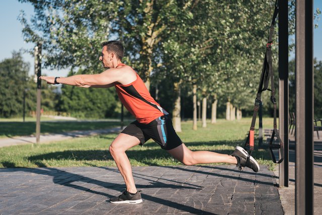 Man doing leg lunges training with trx fitness straps outdoor