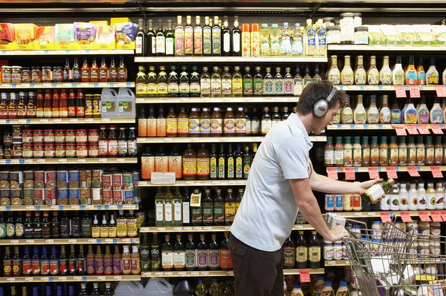 Young man in headphones placing bottle of oil in cart, side view