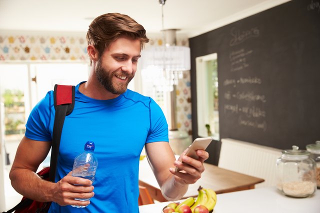 Man wearing gym gear holding a bottle of water in a kitchen