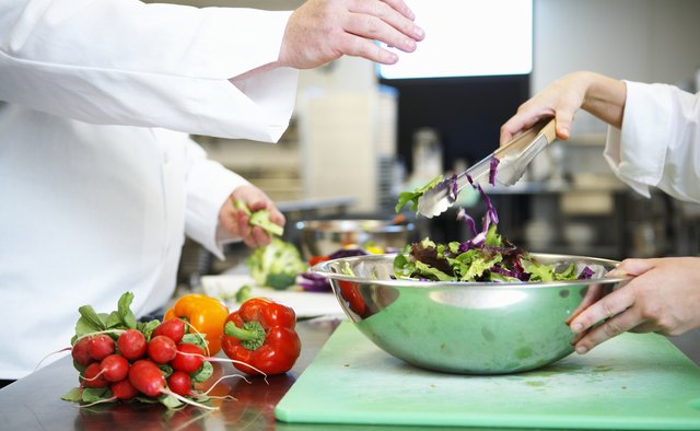 Chefs preparing salad in kitchen, mid section