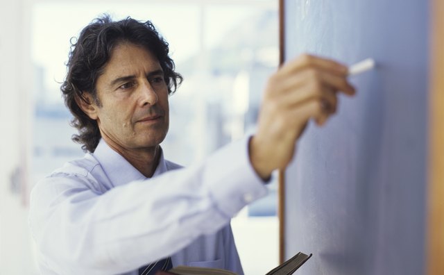 Teacher writing on blackboard and holding book, close up