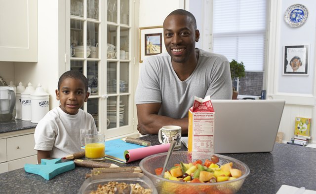 Boy (6-7) drawing at kitchen counter, father sitting beside, portrait
