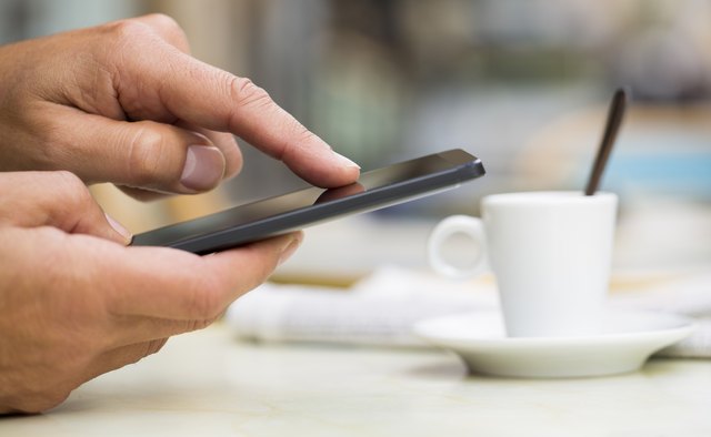 Man using cell phone on cafe terrace, news paper, coffee