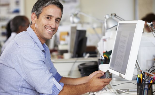 Man Using Mobile Phone At Desk In Busy Creative Office