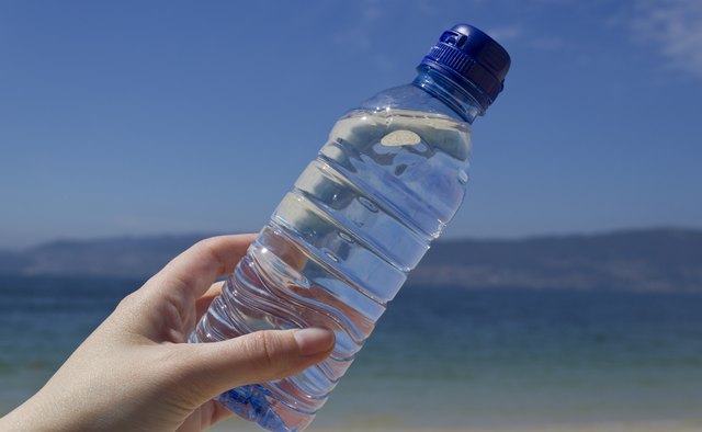 Woman hand with a water bottle on the beach