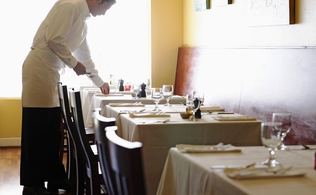 Young man setting tables in restaurant, side view