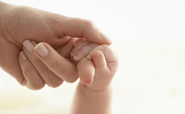 Baby girl (3-6 months) holding woman's finger, close-up
