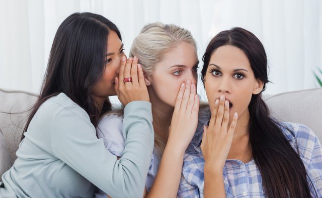 Two friends whispering secret to shocked brunette