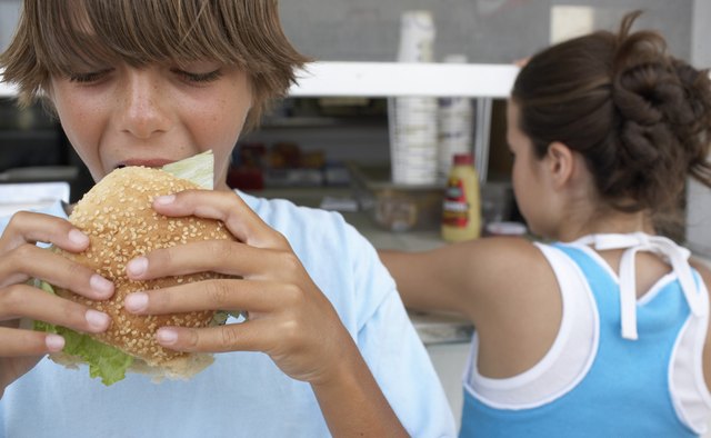 Boy (9-11) eating hamburger, girl (12) queuing at vendor's window
