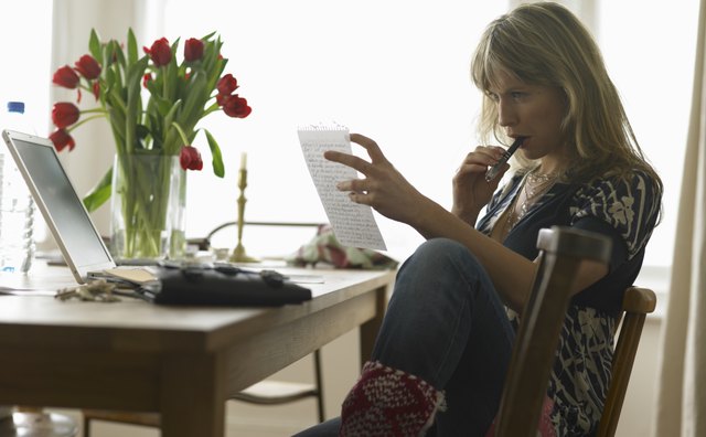 Young woman sitting at dining table reading sheet of paper