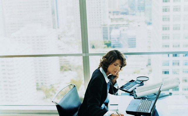 Businesswoman Sitting at Her Desk Using the Phone and Writing in a Notepad
