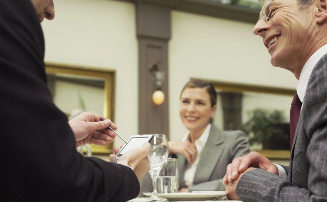 Businesspeople in restaurant smiling at man using electronic organiser