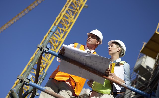 Male and Female Construction Workers Stand on a Platform in a Building Site Discussing a Blueprint