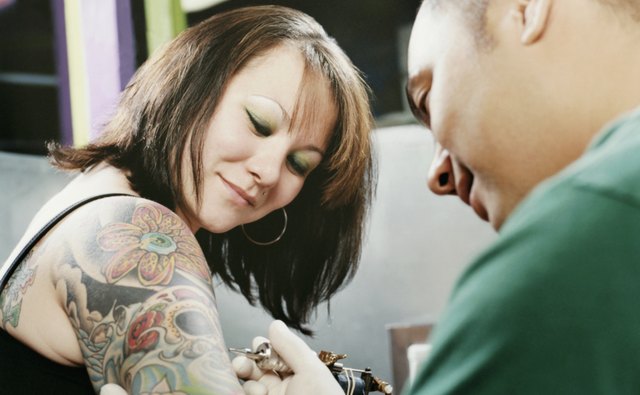 Woman Watching a Tattooist Tattooing Her Arm