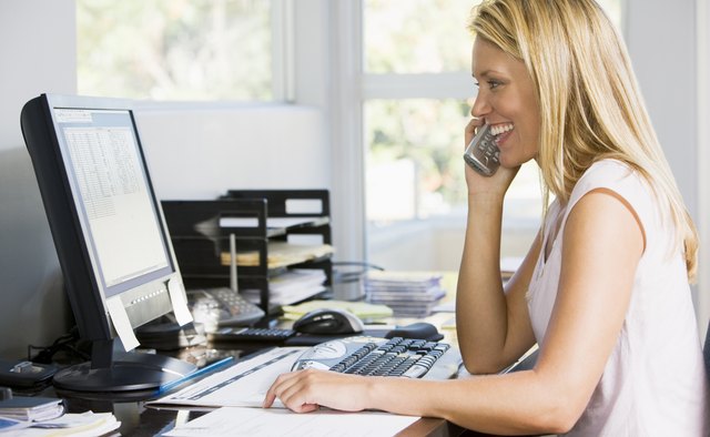 Woman in home office using computer talking on telephone