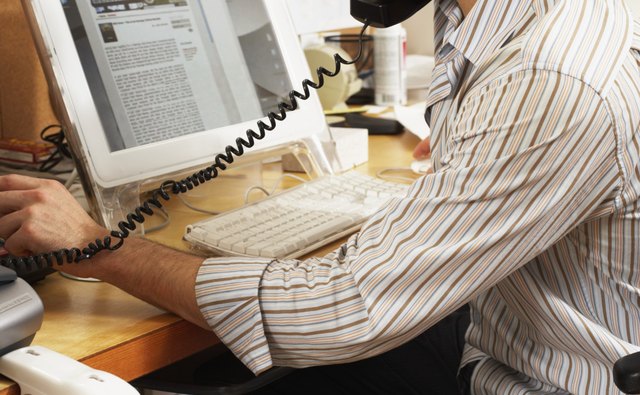 Male office worker balancing phone on shoulder, looking at computer
