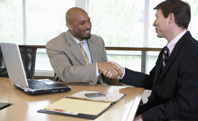Two businessmen shaking hands in boardroom, smiling, side view