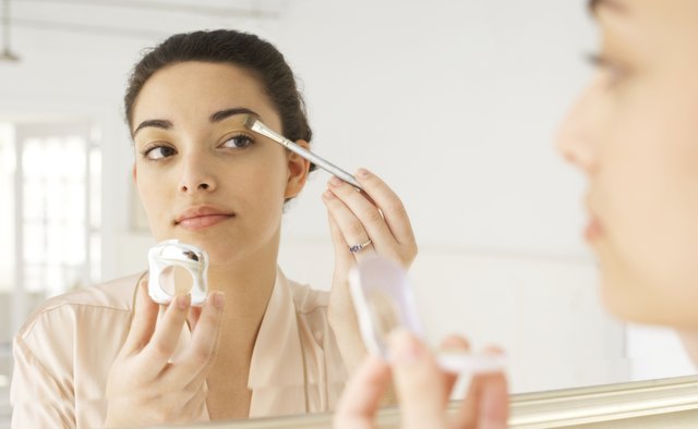 Young woman applying make-up in mirror, using brush, close-up