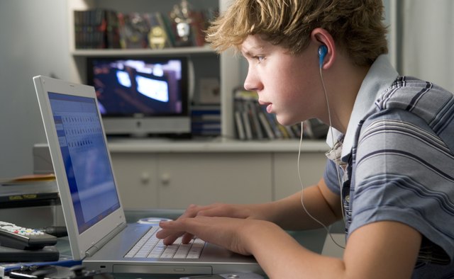 Young boy in bedroom using laptop and listening to MP3 player