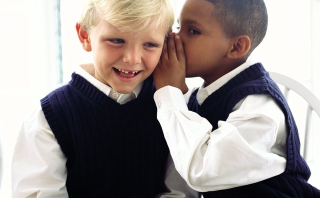 portrait of a boy (8-10) whispering to another at school