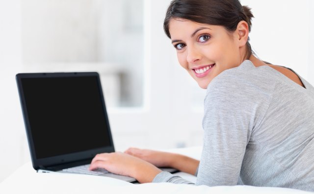 Young woman smiling in bed with a laptop