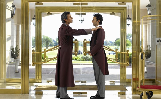 Concierge dusting bellboy's lapel in hotel foyer, side view
