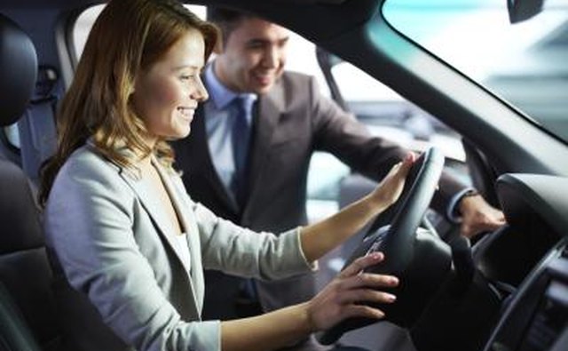 A woman sitting in the driver's seat of a new car with a salesman standing next to her