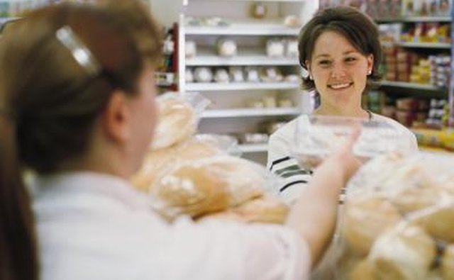 A young woman collecting day old items from a bakery counter.